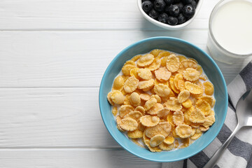 Bowl of tasty corn flakes and blueberries served on white wooden table, flat lay. Space for text