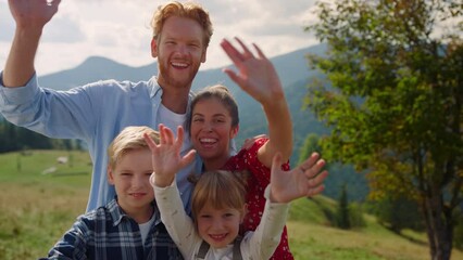 Cheerful family posing camera on green mountains. Parents have fun with kids.