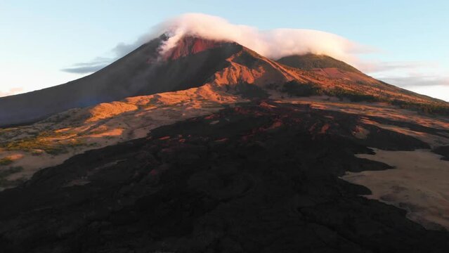 Escena de lava seca y volc&aacute;n activo en erupci&oacute;n cubierto de nubes en el amanecer