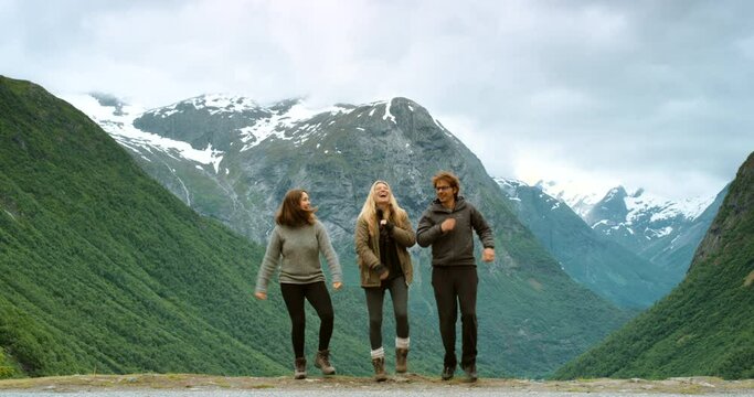 Happy, excited and hiking friends dancing on mountain or snow green hills outdoors with beautiful nature landscape background. Silly and fun tourist woman and man exploring mountains in Stryn Norway