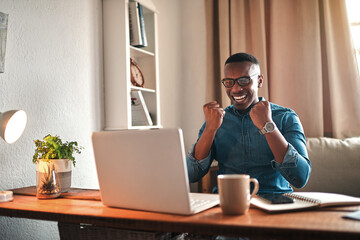 Businessman reading good news on a laptop, looking excited and happy after a loan approval, winning...