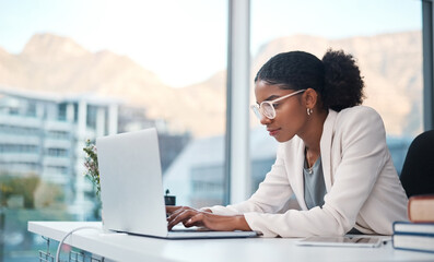 Data professional and secretary typing an email on a laptop and doing online research while working in an office. African entrepreneur looking focused while using the internet for work - Powered by Adobe