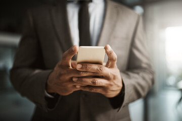 Businessman texting on a phone to send a formal business sms text inside an office at work. African corporate executive professional male wearing a suit typing an email to his client online close up
