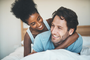 Interracial, playful and loving couple cuddling in bed and enjoying the weekend together at home....