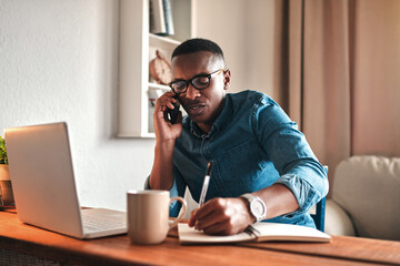 Young serious professional businessman talking on phone call, writing and sitting with digital...