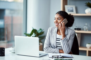 Business woman talking on phone call or young entrepreneur answering cellphone in front of laptop in work office. Happy, African American female smiling and receiving good news while sitting at desk.