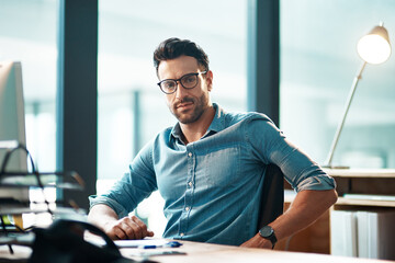 Creative entrepreneur working on computer in office after researching, browsing or searching online for startup company ideas. Portrait of confident, serious or ambitious business man sitting at desk