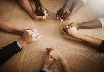Obraz na płótnie Canvas Group of diverse business people holding their hands together in solidarity on a table. Colleagues in unity supporting one another, prayer in the office space between co workers.