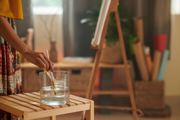 Cropped image of artist cleaning brush in water to get rid of paint