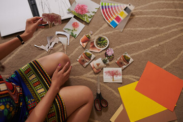 Cropped image of creative woman sitting on floor and cutting out varioius pictures for collage