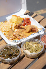 A view of a styrofoam container of soul food, featuring smothered chicken, green beans and candied yams.