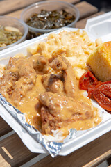 A view of a styrofoam container of soul food, featuring smothered chicken, green beans and candied yams.