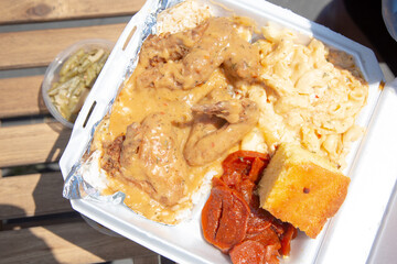 A top down view of a styrofoam container of soul food, featuring smothered chicken.