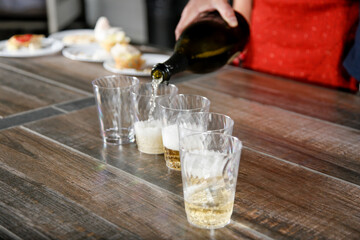 A view of a person pouring sparkling wine into plastic cups, at a party setting.