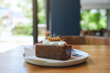 A piece of carrot cake in a white plate on wooden table