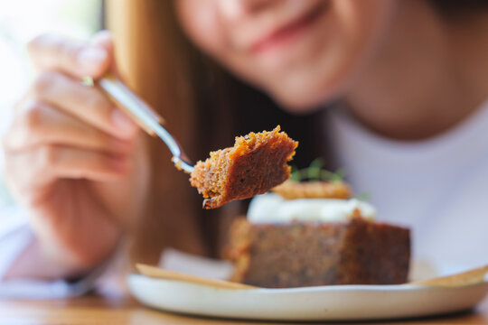 Closeup image of a young woman eating and showing a piece of carrot cake with fork