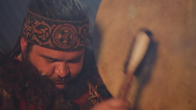 Ecstatic obese man taps shamanic drum doing old mystical ritual in ail closeup. Shamanic traditions of Siberia. Amazing Altai ethnic culture
