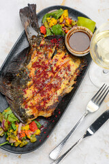 fried fish cut on a plate with salad and sauce on a white background with a glass of wine macro photo
