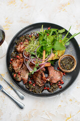 grilled meat loin in a plate with greens and pineapple grilled on a white background with a glass of wine vertical photo
