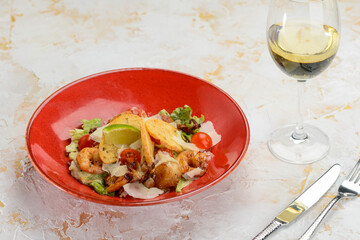 salad with seafood in a red plate on a white background with a glass of wine
