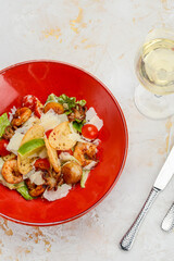 salad with seafood in a red plate on a white background with a glass of wine vertical photo
