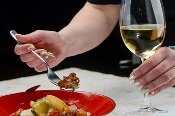 small baby octopus on a fork in female hands and a glass of wine
