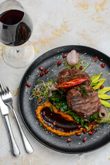 grilled meat steak on a black plate with salad and sauce on a white background
