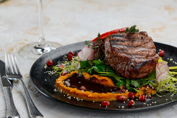 grilled meat steak on a black plate with salad and sauce on a white background macro photo
