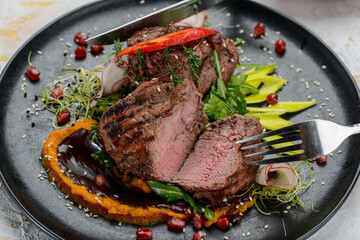 steak meat grilled on a black plate with salad is cut with utensils in female hands macro photo
