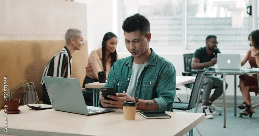 Poster Happy business man texting on a phone while working on a laptop in a busy office. Smiling young professional chatting online while sending an email, excited about a social network app on the internet