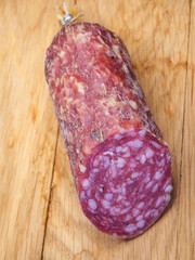 Half a stick of smoked sausage on a wooden surface. A close-up picture.