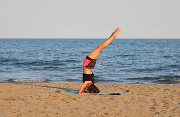 young slender girl performs gymnastic exercises by the sea in summer with short shorts