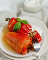 Peppers stuffed with rice and meat, garnished with basil on a light plate with cutlery, close-up on a light background with a linen tablecloth