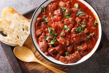 Moelas Guisadas slowly stewed chicken gizzards in tomato sauce close-up in a bowl on a wooden tray on the table. horizontal top view from above
