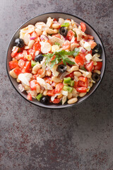 Summer cod salad with white beans, eggs and vegetables close-up in a bowl on the table. Vertical top view from above