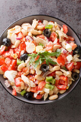 Spanish cod salad Empedrat with white beans, eggs and vegetables close-up in a bowl on the table. Vertical top view from above