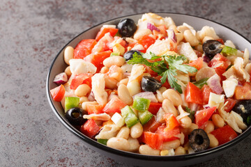 Traditional empedrat Beans salad with shredded salt cod, tomatoes, bell peppers, onions, eggs and black olives close-up in a bowl on the table. horizontal