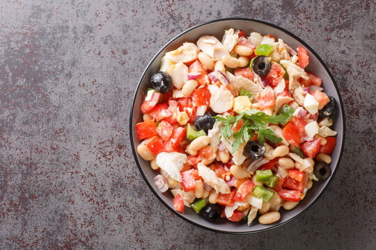Spanish empedrat white Beans salad with cod, tomatoes, bell peppers, onions, eggs and black olives close-up in a bowl on the table. horizontal top view from above