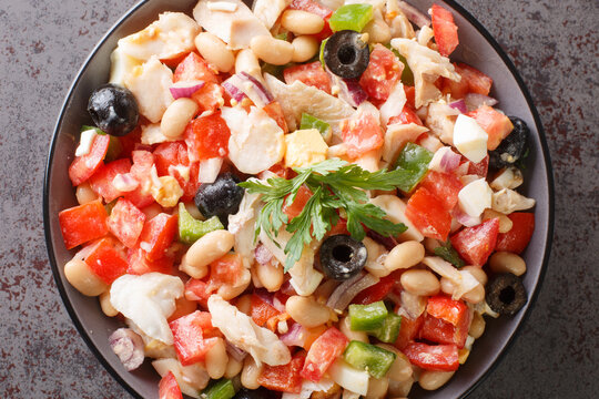 Traditional empedrat Beans salad with shredded salt cod, tomatoes, bell peppers, onions, eggs and black olives close-up in a bowl on the table. horizontal top view from above