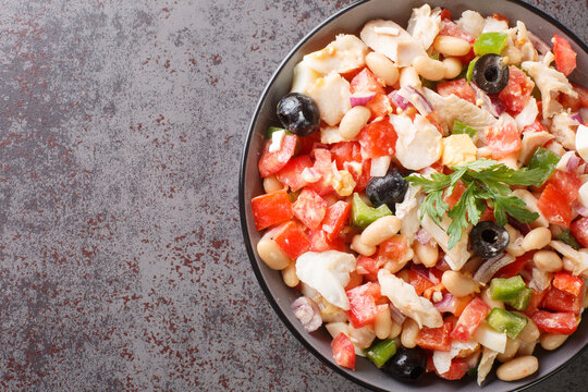 Mediterranean homemade cod salad with white beans, eggs and vegetables close-up in a bowl on the table. horizontal top view from above