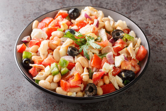 Spanish empedrat white Beans salad with cod, tomatoes, bell peppers, onions, eggs and black olives close-up in a bowl on the table. horizontal