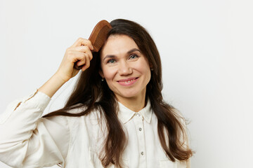 joyful happy woman combing her hair with a wooden comb smiling joyfully. Horizontal photo on a light background