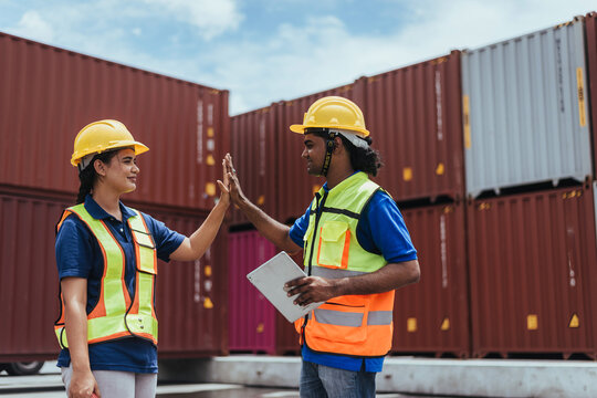 Industrial Engineer giving high five to colleague in Logistic center. Asian Indian workers wearing safety vests to working about shipment in Container terminal, Working in Storage Distribution Center.