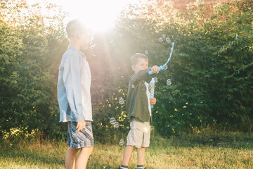 Boys play with soap bubbles in a summer park, Among the greenery. Happy children catch soap bubbles.