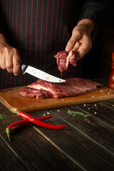 Butcher or chef cuts raw fresh beef meat on a cutting board before baking or barbecue. Working environment in the kitchen of a restaurant or hotel.