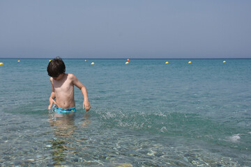 Child playing and swimming in the sea. Boy splashing in a water on hot sunny day