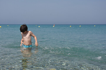 Child playing and swimming in the sea. Boy splashing in a water on hot sunny day