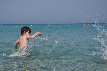 Child playing and swimming in the sea. Boy splashing in a water on hot sunny day