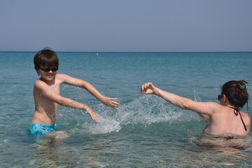 40 Years old Mom play with son in the sea. Cheerful child splashing and enjoy in water with his mother