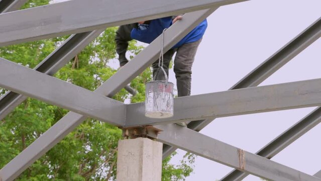 A painter is painting a steel roof without wearing safety equipment.